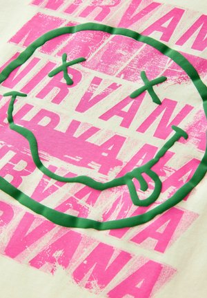 Vaalea kerma kangas, jossa on suuri vihreä hymyilevä kasvot -kuvio, joka on ääriviivoitettu teksturoidulla neonpinkillä ja päällekkäin "Nirvana"-teksti.