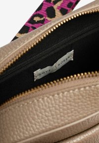Borsa a mano beige con texture e cerniera dorata, dotata di un interno nero e un'etichetta con la scritta "Love & Roses". Cinghia con stampa leopardata colorata visibile.