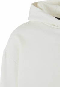 Sweatshirt à capuche blanche, fabriquée dans un tissu doux, avec un design décontracté et une apparence simple et épurée. La capuche repose à plat contre le cou.
