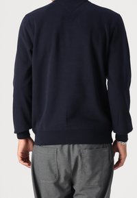 Sweatshirt bleu marine à col rond, avec des poignets et un ourlet côtelés, associé à un pantalon gris avec des poches arrière et un détail de logo.