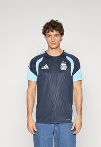Navy and light blue sports jersey made of textured fabric, featuring a round neck, short sleeves, and a central badge with Argentine emblem.