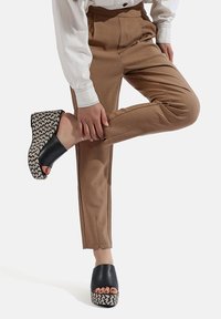 Sandali platform neri con un motivo intrecciato sul tallone, abbinati a pantaloni beige su misura con una vestibilità slim e pieghe sottili.