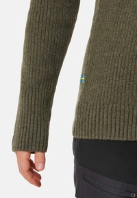 Olive green ribbed knit sweater with a textured finish. Features a small blue and yellow country flag on the side hem.