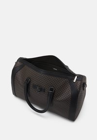 Sac de voyage en toile marron à motifs avec des accents en cuir noir, deux poignées et une fermeture éclair. Dispose d'un intérieur spacieux avec des poches supplémentaires.
