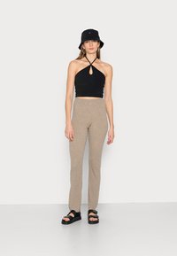 Top halter preto com detalhe de fenda, combinado com calças de malha canelada em bege claro. Um chapéu bucket preto e sandálias pretas de tiras complementam o visual.