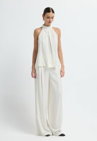 Haut à bretelles blanc avec un design drapé, associé à un pantalon large blanc. Les deux pièces présentent une texture lisse et des accents minimalistes. Chaussures noires.