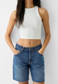 Top corto blanco acanalado combinado con pantalones cortos de mezclilla azul claro de talle alto, con dobladillo sin rematar y bolsillos frontales.