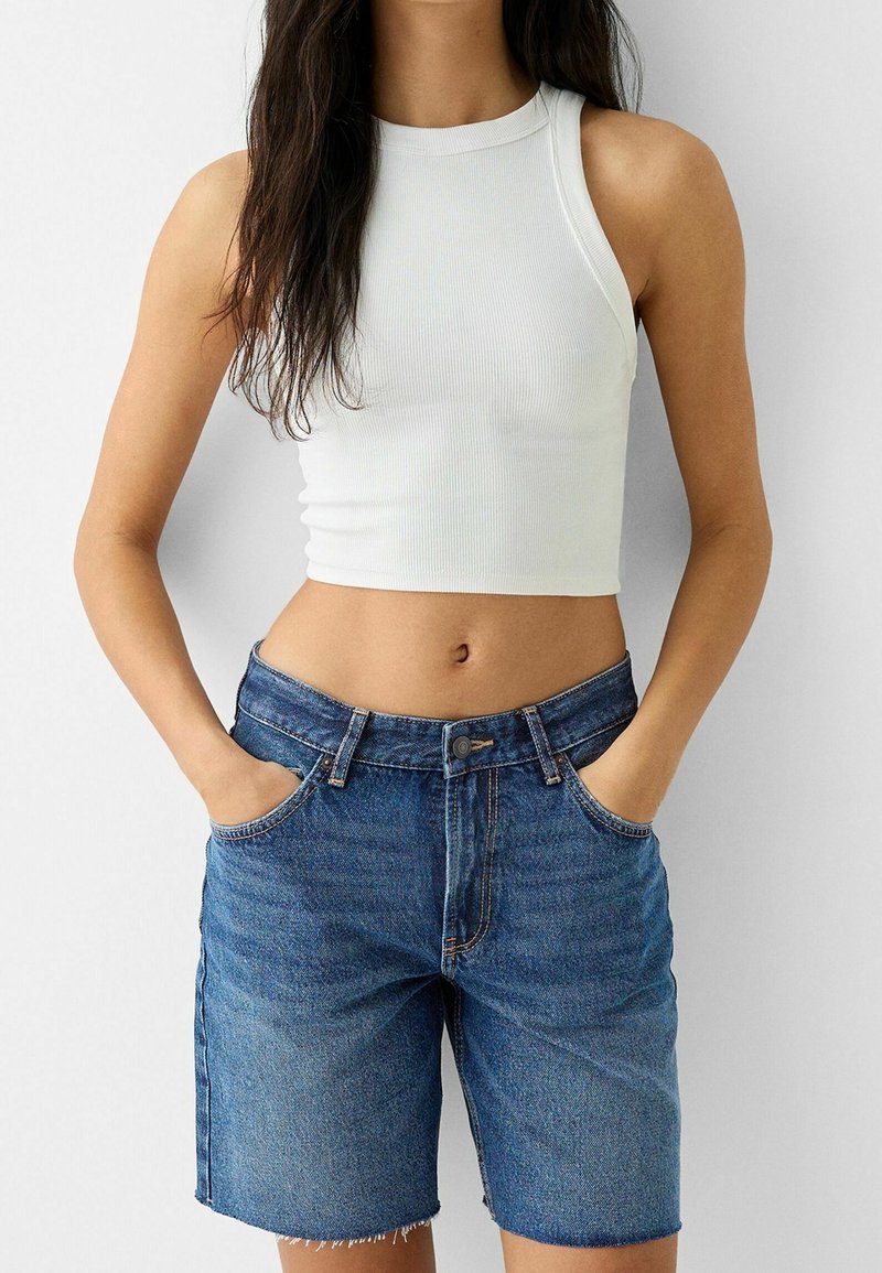 Top corto blanco acanalado combinado con pantalones cortos de mezclilla azul claro de talle alto, con dobladillo sin rematar y bolsillos frontales.