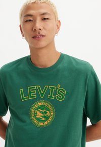 Grønn bomull t-skjorte med rund hals og en stor gul Levi's-logo med et sirkulært grafisk design på forsiden.