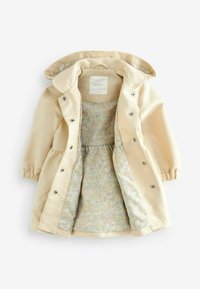 Veste imperméable beige avec capuche, dotée de boutons-pression et de poignets élastiques. Doublure à motif floral aux couleurs pastel visible.