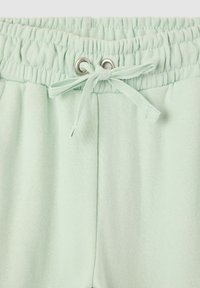 Jasnozielone spodnie z elastycznym paskiem w talii, z materiałową kokardą przewleczoną przez dwa srebrne oczka.