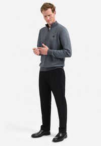 Donkergrijze pullover met een ritskraag en gestructureerde stof, gecombineerd met zwarte broek en glanzende zwarte laarzen, wat een moderne casual uitstraling benadrukt.
