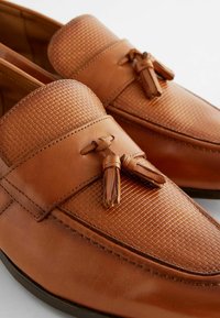 Mocassins en cuir tan avec une texture tissée sur le dessus et des franges décoratives. Fini lisse avec des coutures contrastées.