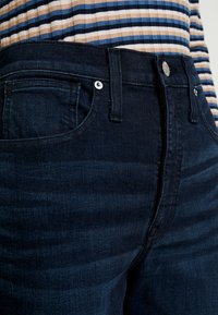 Mörk denimjeans med en figurnära design, som har en enkel framficka, silvrig knappdetalj och en slät yta.