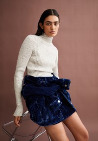 Romige turtleneck trui van een wolmix met ribbelstructuur, in combinatie met een donkerblauwe corduroy rok met een ceinture-detail.