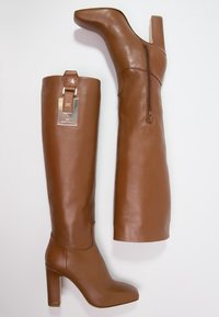 Brązowe skórzane kozaki za kolano z kwadratowym obcasem, zamkiem błyskawicznym po boku i ozdobną klamrą u góry. Gładka tekstura i smukły design.