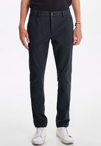 Donkergrijze broek met een gladde textuur, rechte pasvorm, voorkruiszakken en een knoopsluiting, gecombineerd met witte sneakers.