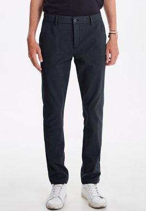 Donkergrijze broek met een gladde textuur, rechte pasvorm, voorkruiszakken en een knoopsluiting, gecombineerd met witte sneakers.