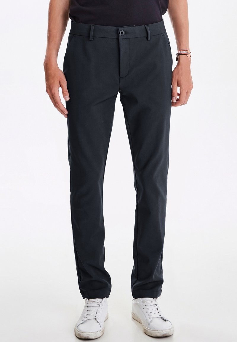 Donkergrijze broek met een gladde textuur, rechte pasvorm, voorkruiszakken en een knoopsluiting, gecombineerd met witte sneakers.