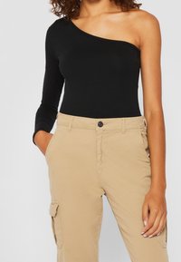 Musta olkaimeton bodysuit, joka on valmistettu joustavasta kankaasta, yhdistettynä vaaleanruskeisiin cargo-housuihin, joissa on sivutaskut ja nappikiinnitys.