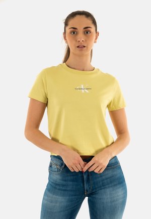 T-shirt in cotone giallo con colletto a girocollo, maniche corte e stampa logo bianca sul lato sinistro. Abbinato a jeans in denim blu.