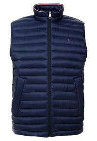 Marinblå puffer-väst med hög krage, dragkedja, horisontellt quiltat mönster och kontrasterande röda och vita detaljer vid kragen.