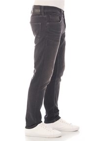 Vaqueros de mezclilla de color gris oscuro con un ajuste slim, diseño de cinco bolsillos y un leve desgaste. Parche del logo en la cinturilla. Combinados con zapatillas blancas.