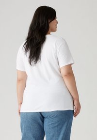 Λευκό βαμβακερό κοντομάνικο T-shirt με στρογγυλή λαιμόκοψη, άνετη εφαρμογή και casual στυλ, συνδυασμένο με ανοιχτό μπλε τζιν παντελόνι.