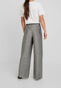 Wijd-gesneden broek in glanzend zilver materiaal, met een zachte textuur en hoge taille, gecombineerd met een eenvoudig grijs T-shirt en zwarte sneakers.