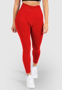 Rote hoch taillierte Leggings aus dehnbarem Stoff, mit glatter Textur und figurbetontem Schnitt, kombiniert mit weißen Sportschuhen.