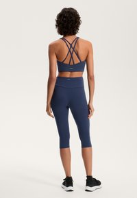 Temno modra športna obleka z športnim modrčkom z nazaj v obliki križa in legicami do sredine meč. Narejena iz gladkega, raztegljivega materiala.