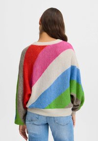 Pull surdimensionné coloré en tissu tricot doux, présentant des rayures diagonales rouge, rose, bleu, vert et beige. Poignets et ourlet côtelés.