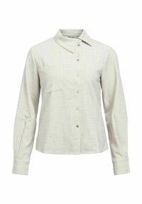 Chemise à manches longues beige clair avec boutons, col pointu et détail discret de poche poitrine sur fond blanc.