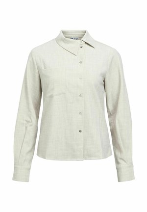 Chemise à manches longues beige clair avec boutons, col pointu et détail discret de poche poitrine sur fond blanc.