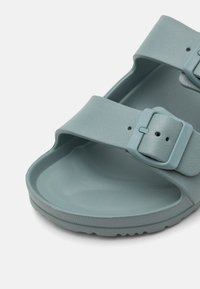 Šviesiai žalia chalė su dviem reguliuojamais dirželiais ir sagtimis. Pagaminta iš tekstūrinės plastiko, su kontūruota pėdos dalimi ir tekstūruotu padu.