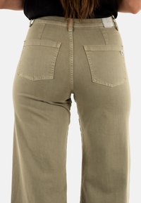 Pantaloni a gamba larga di colore verde oliva con un tessuto testurizzato, dotati di due tasche posteriori e un accento a forma di cuore sulla tasca destra.