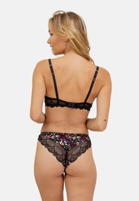 Soutien-gorge en dentelle noire avec des bretelles ajustables, associé à une culotte noire à motif floral coloré avec des bords festonnés.