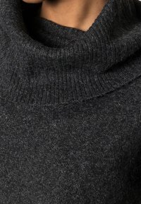 Kolgrå, mjuk stickad tröja med en hög, ribbad krage. Det strukturerade tyget har subtila fläckar som ger en mysig känsla.