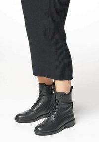 Stivaletti neri in pelle con design a lacci, dettagli con zip e tacco basso a blocco. Materiale testurizzato e tomaia leggermente abrasata.