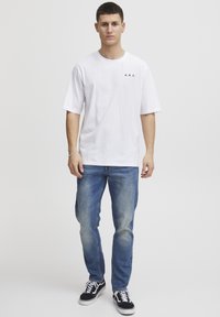 Hvid bomulds t-shirt med sort "A.R.C." logo, parret med lysblå denim jeans og sorte sneakers med hvide såler og snørebånd.