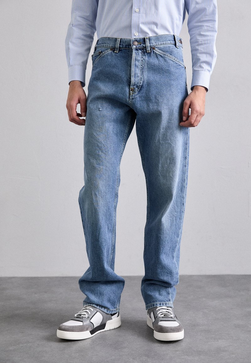 Jeans din denim de culoare albastru deschis, cu o croială lejeră, având un fermoar cu nasture, cinci buzunare și o ușoară decolorare. Asortați cu adidași gri sport.