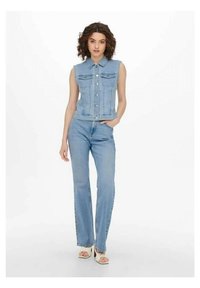 Vest de denim cu mâneci scurte, culoare bleu deschis, cu închidere pe butoane, două buzunare pe piept, asortat cu blugi drepti bleu deschis și încălțăminte deschisă.