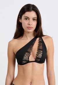 Sostén negro con un diseño asimétrico, con encaje en el escote pronunciado, tejido suave y sin adornos adicionales.