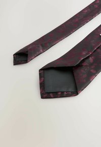 Tmavo kvetinový vzorovaný kravata s odtieňmi tmavej burgundskej a čiernej, vyrobená z jemnej látky; má špicaté konce a pevné pozadie.