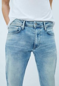 Vaaleansiniset farkut, joissa on kulutettu pinta, viisi taskua ja metalliset yksityiskohdat vyötäröllä ja taskuissa.