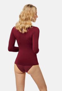 Top de manga larga en color burdeos con una tela suave y elástica. El diseño presenta un cuello redondo y una silueta ajustada, combinado con braguitas a juego.