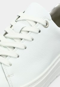 Λευκό δερμάτινο αθλητικό παπούτσι με στρογγυλεμένη μύτη, υφασμένη επιφάνεια, επίπεδα κορδόνια και μεταλλικά οφθαλμικά κουμπώματα· διαθέτει κομψό σχεδιασμό και διακριτικό ραφές.