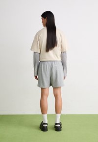 Un tricou scurt bej deasupra unor pantaloni scurți gri, cu pantofi negri și șosete albe. Mâneci lungi rayate vizibile la manșete. Textură de țesătură netedă.