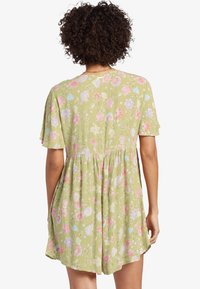 Vestido floral verde con mangas cortas, cintura fruncida y una tela ligera y texturizada con patrones de flores en rosa y azul.