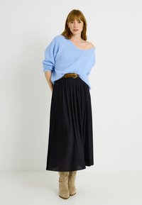 Pull en tricot surdimensionné bleu clair avec des manches longues. Jupe maxi plissée noire avec une ceinture marron ornée d'une boucle métallique ronde. Bottes beige jusqu'aux genoux.